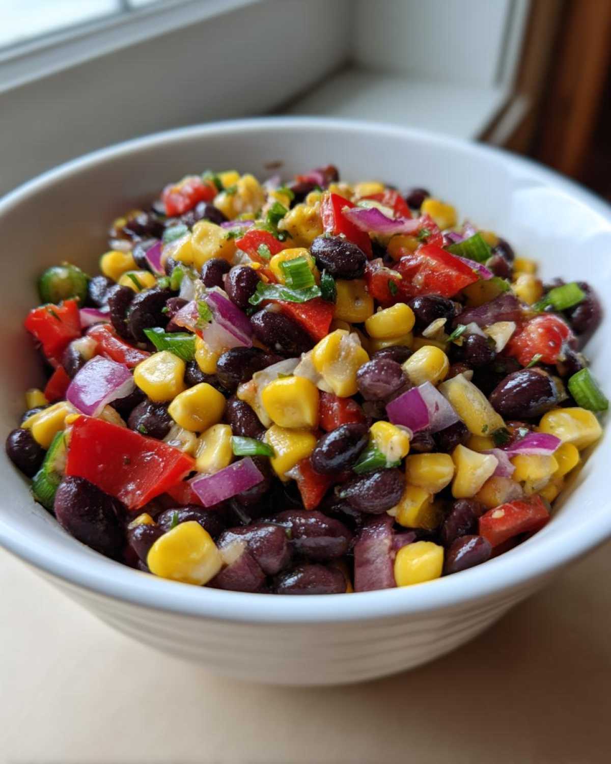 Close-up of vibrant cowboy caviar featuring black beans, yellow corn, red peppers, and red onion in a white bowl.