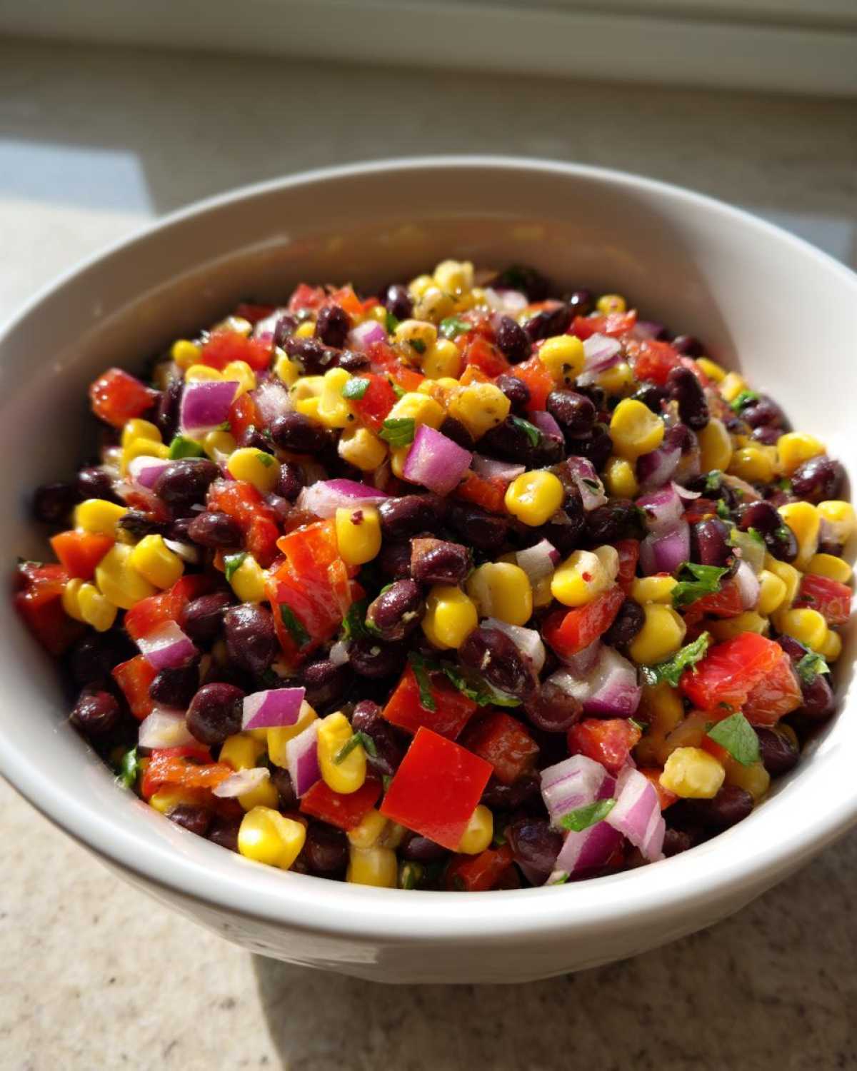 Close-up of colorful cowboy caviar dip featuring black beans, corn, red onion, and tomatoes in a white bowl.