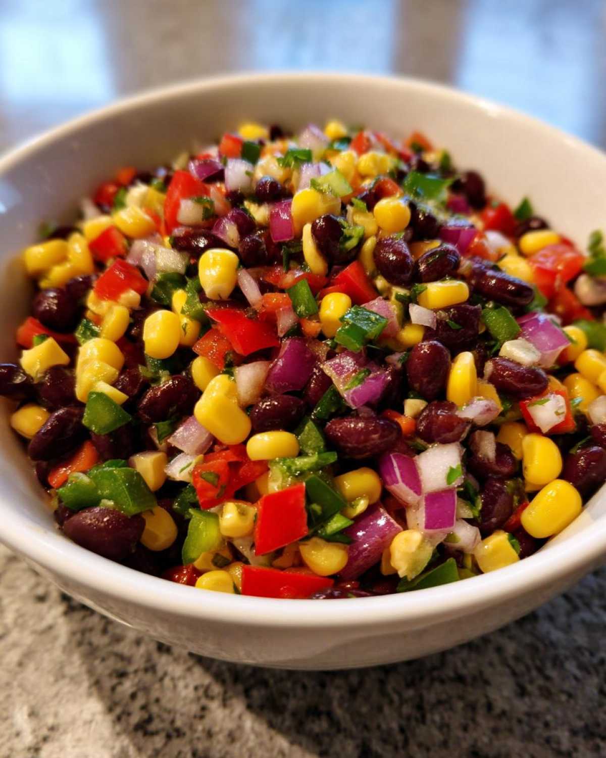 Close-up of a white bowl filled with colorful cowboy caviar featuring black beans, corn, red onion, and peppers.