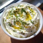 A close-up of a bowl of fluffy whipped feta dip, drizzled with golden olive oil and sprinkled with fresh dill.