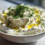 Close-up of a bowl of creamy whipped feta dip drizzled with olive oil and fresh dill.