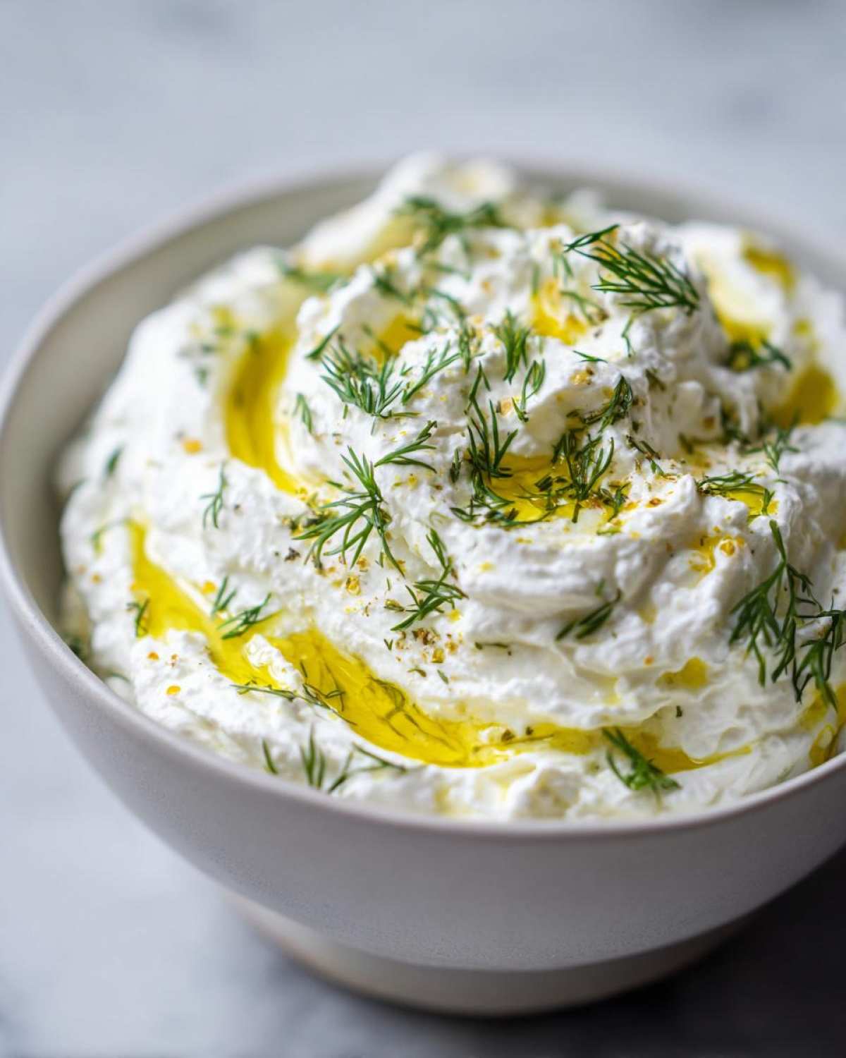 Close-up of creamy whipped feta dip in a bowl, drizzled with olive oil and fresh dill.