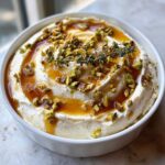 A bowl of creamy whipped goat cheese topped with drizzled honey, chopped pistachios, and fresh thyme.