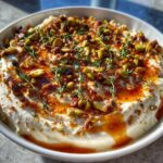 A bowl of creamy whipped goat cheese topped with chopped pistachios, chili oil, and fresh thyme sprigs.