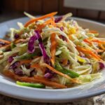 Close-up of a vibrant cabbage salad with shredded white and red cabbage, carrots, and green peppers in a white bowl.