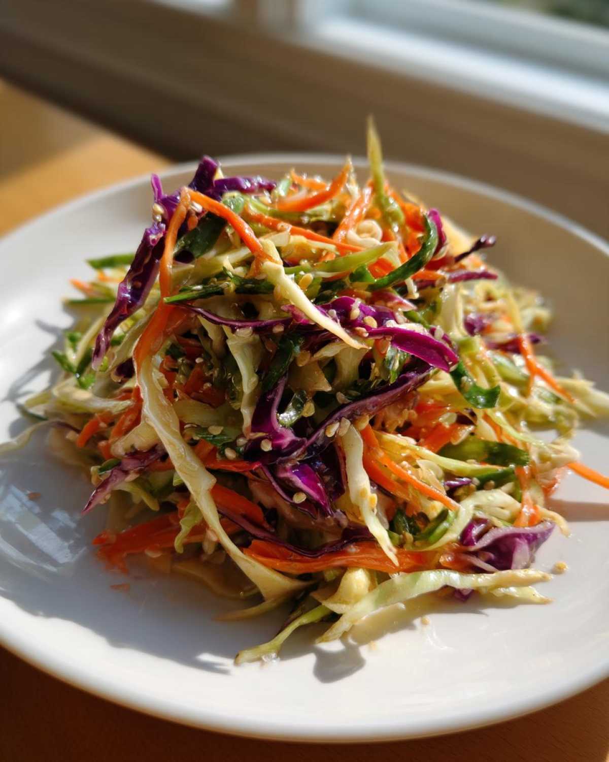 A close-up of a vibrant, colorful cabbage salad featuring shredded green and purple cabbage, carrots, and sesame seeds.