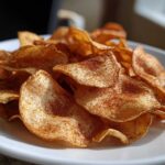 Close-up of crispy Air Fryer Cinnamon Sugar Apple Chips dusted heavily with cinnamon and sugar mix on a white plate.