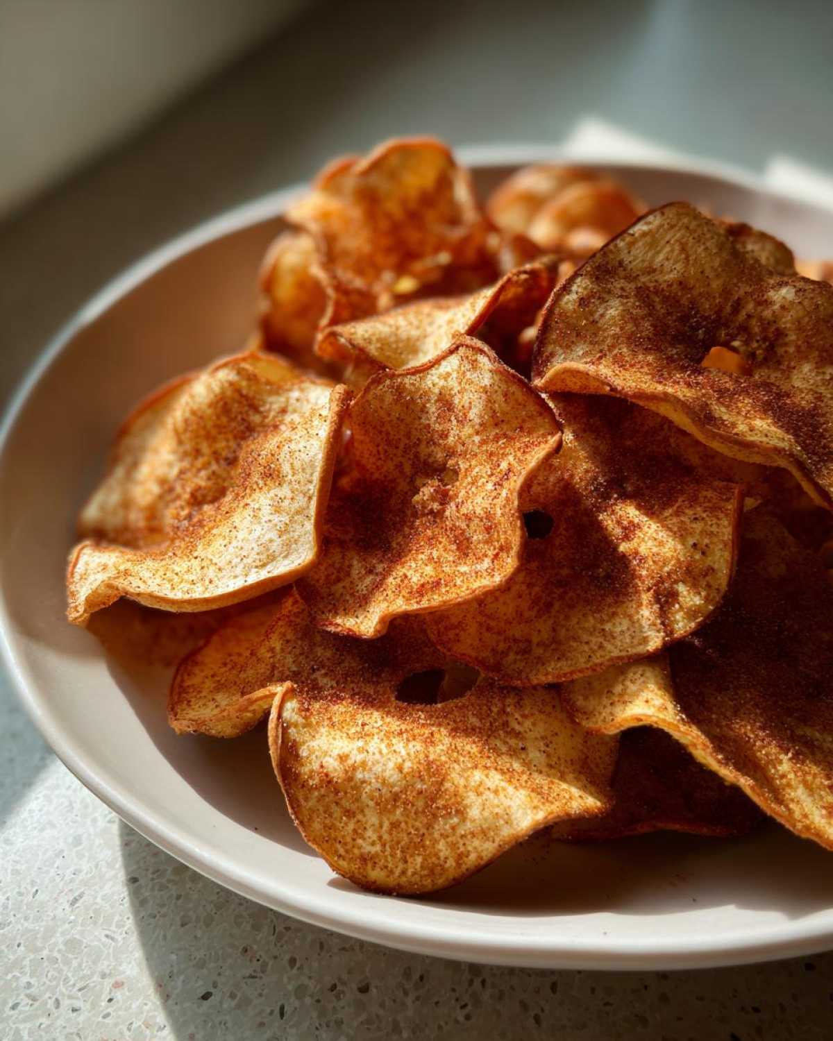 Close-up of crispy Air Fryer Cinnamon Sugar Apple Chips piled high in a light-colored bowl.