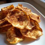 Close-up of crispy Air Fryer Cinnamon Sugar Apple Chips piled on a white plate, dusted heavily with spice.