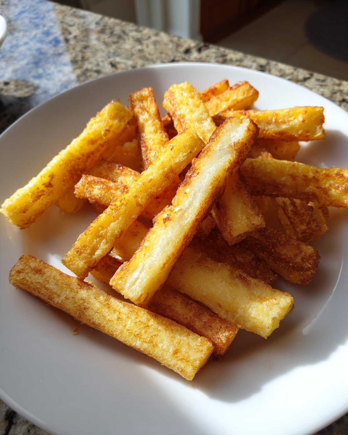 A pile of golden brown Air Fryer Crispy Polenta Fries served on a white plate under bright light.