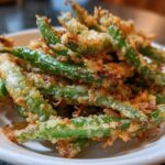 Close-up of a pile of Air Fryer Crispy Tempura Green Beans on a white plate.