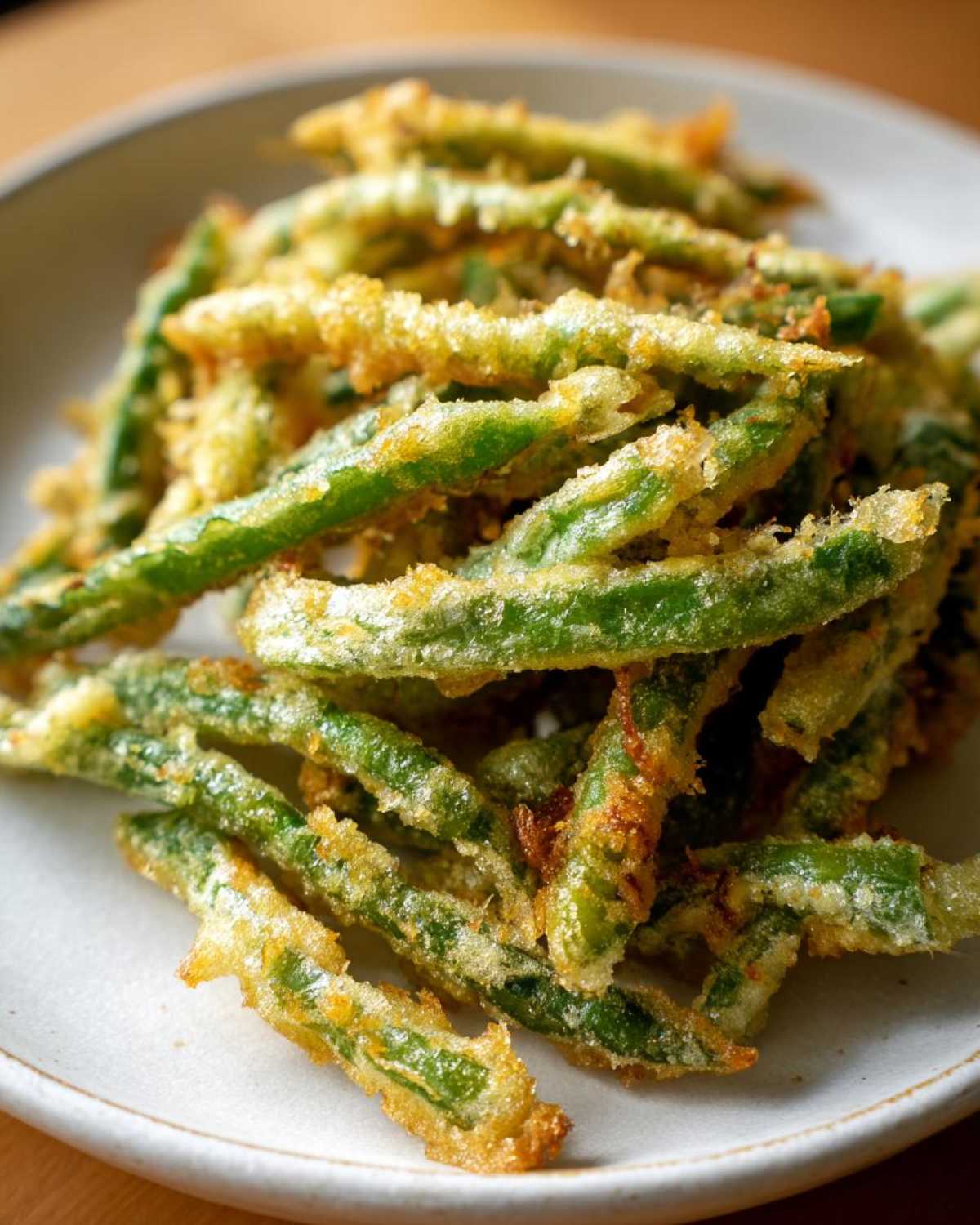 A close-up of perfectly cooked Air Fryer Crispy Tempura Green Beans piled on a light-colored plate.