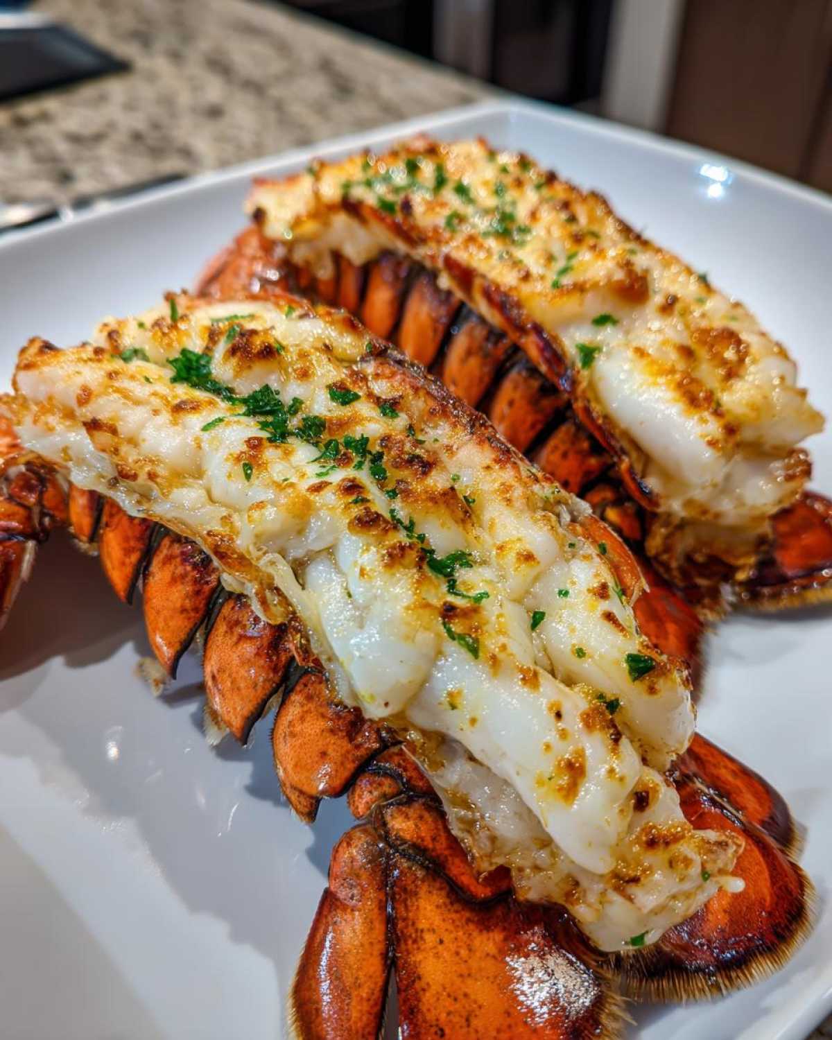 Two cooked Air Fryer Garlic Butter Lobster Tails, split open and topped with browned garlic butter and parsley, resting on a white plate.