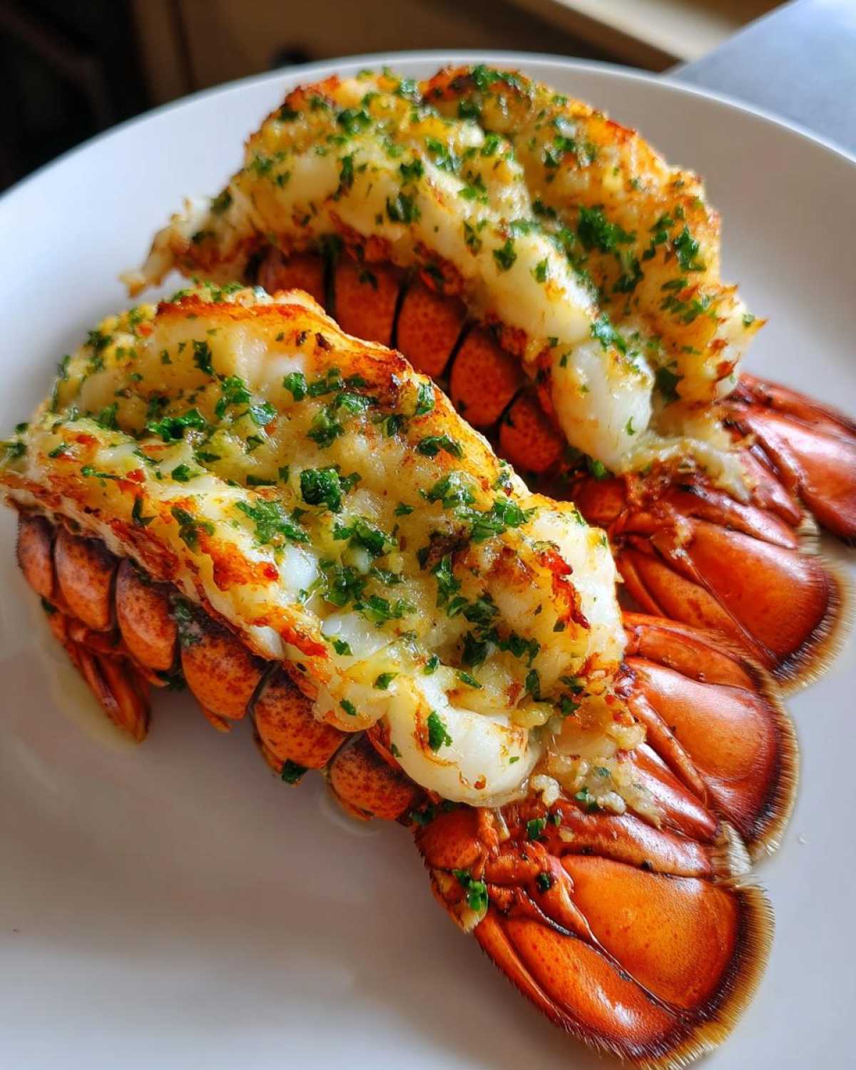 Two cooked Air Fryer Garlic Butter Lobster Tails served on a white plate, topped with melted butter and parsley.