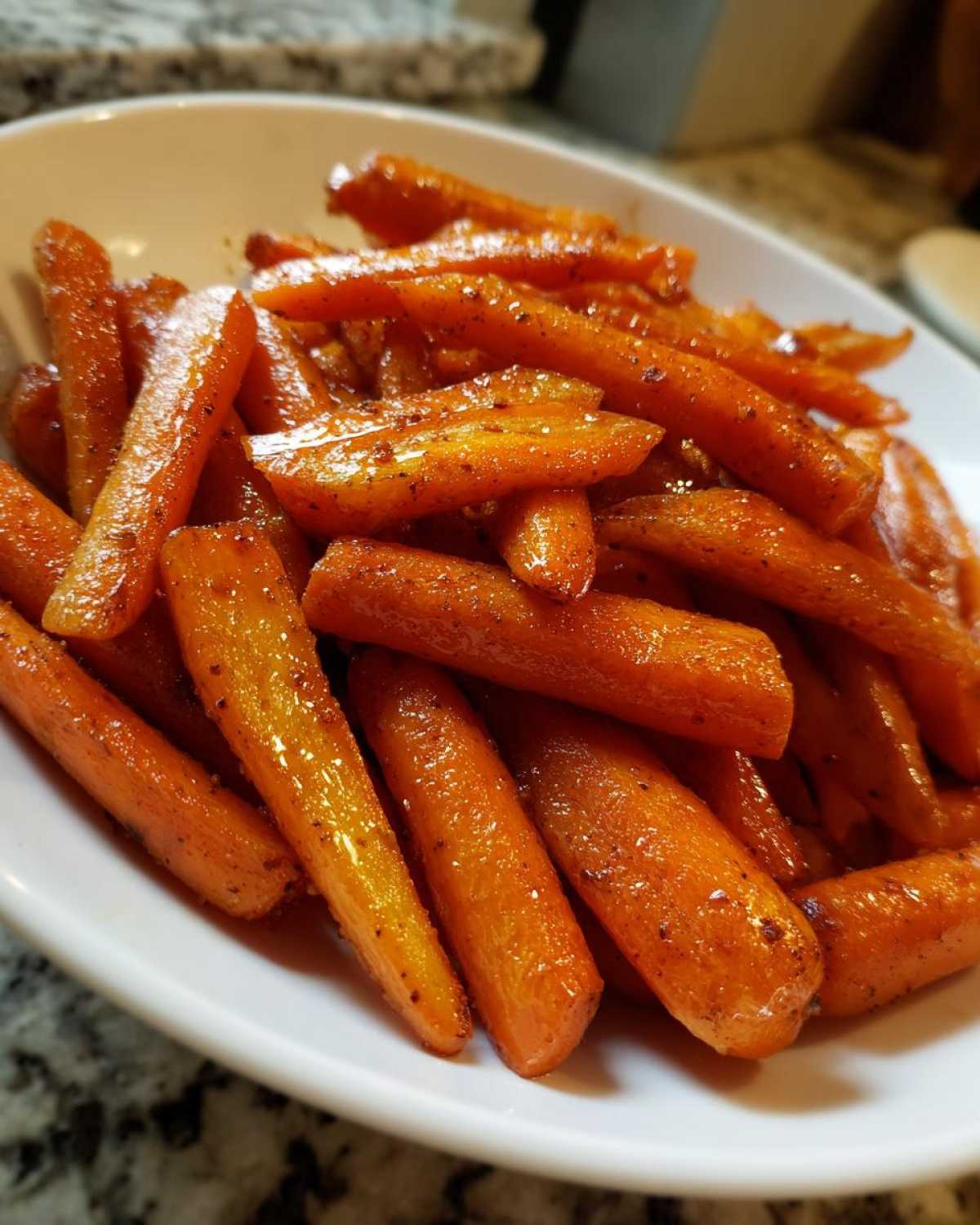 A white bowl filled with glossy, bright orange Air Fryer Maple Glazed Carrots, seasoned with spices.