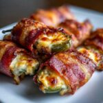 Close-up of crispy, bacon-wrapped Air Fryer Stuffed Jalapeno Poppers oozing with melted cheese.