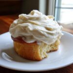 A close-up of a cinnamon roll generously topped with thick Copycat Cinnabon Cream Cheese Frosting on a white plate.