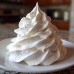 A tall, perfectly piped swirl of thick, white Copycat Cinnabon Cream Cheese Frosting on a small white plate.