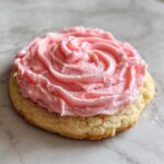 A single, thick Copycat Crumbl Sugar Cookie topped with thick, pink frosting swirled like a rose.