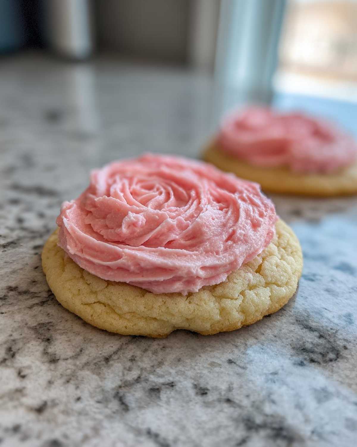 A close-up of a thick, soft Copycat Crumbl Sugar Cookie topped with thick, pink frosting swirled like a rose.