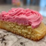 Cross-section of a Copycat Crumbl Sugar Cookie showing the soft base and thick swirl of bright pink frosting.