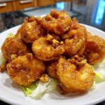 A close-up of golden, glazed shrimp topped with walnuts, served over lettuce, resembling Copycat Panda Express Honey Walnut Shrimp.