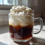 A glass mug filled with dark iced coffee topped generously with thick Copycat Starbucks Vanilla Sweet Cream Cold Foam.