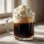 A glass mug filled with dark coffee topped with vanilla sweet cream cold foam and whipped cream.