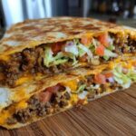 A cross-section view of a homemade Copycat Taco Bell Crunchwrap Supreme showing seasoned beef, melted cheese, lettuce, and tomatoes.