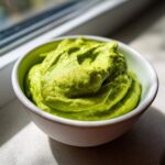 A close-up of vibrant green, thick Creamy Avocado Cilantro Sauce swirled in a small white bowl.