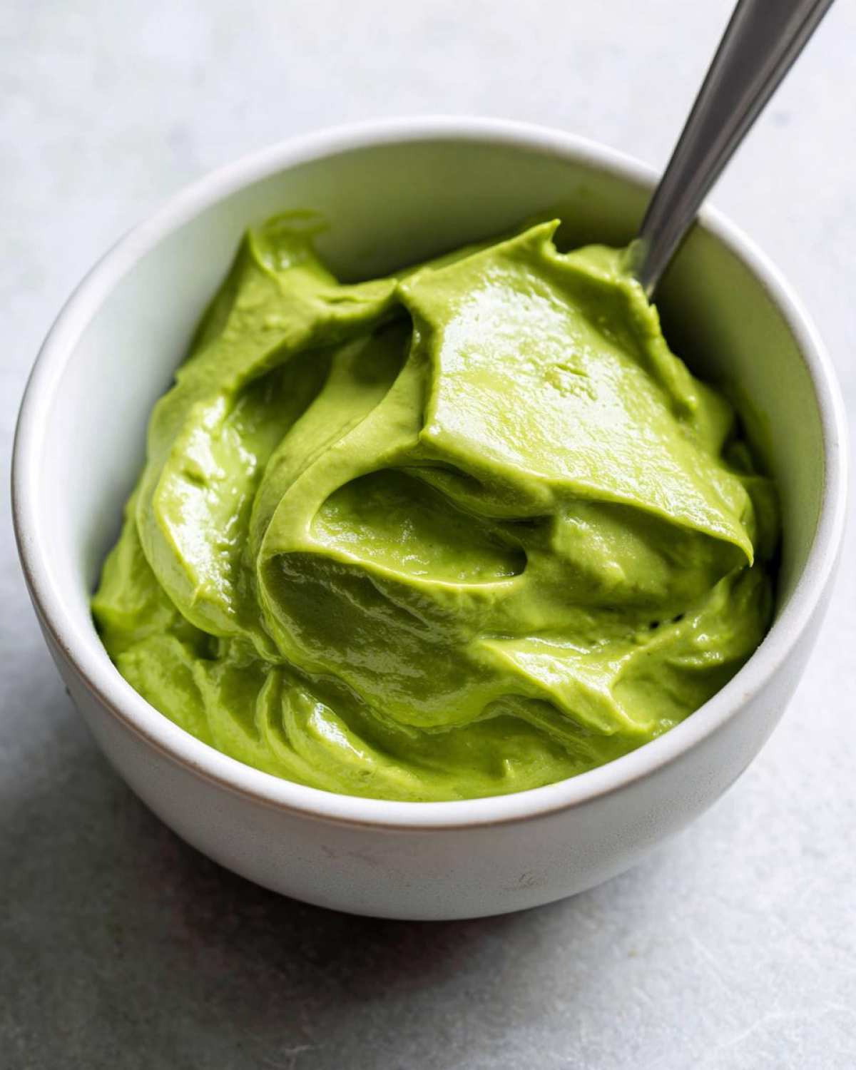 Close-up of vibrant green Creamy Avocado Cilantro Sauce texture in a small white bowl with a spoon.