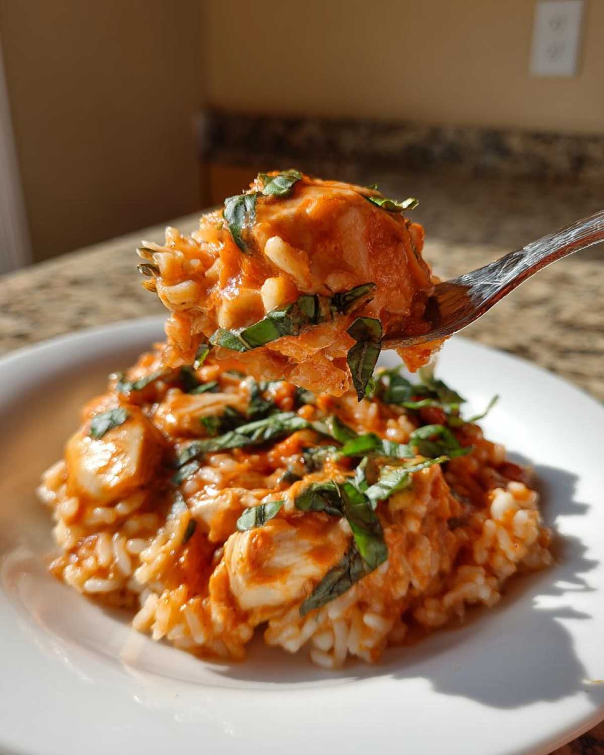 A fork lifts a bite of One-Pot Creamy Tomato Basil Chicken and Rice topped with fresh basil.