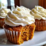 Close-up of a Gluten-Free Carrot Cake Cupcake with cream cheese frosting, showing a bite taken out.