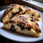 Three wedges of freshly baked Gluten-Free Chocolate Chip Scones, topped with coarse sugar, served on a white plate.