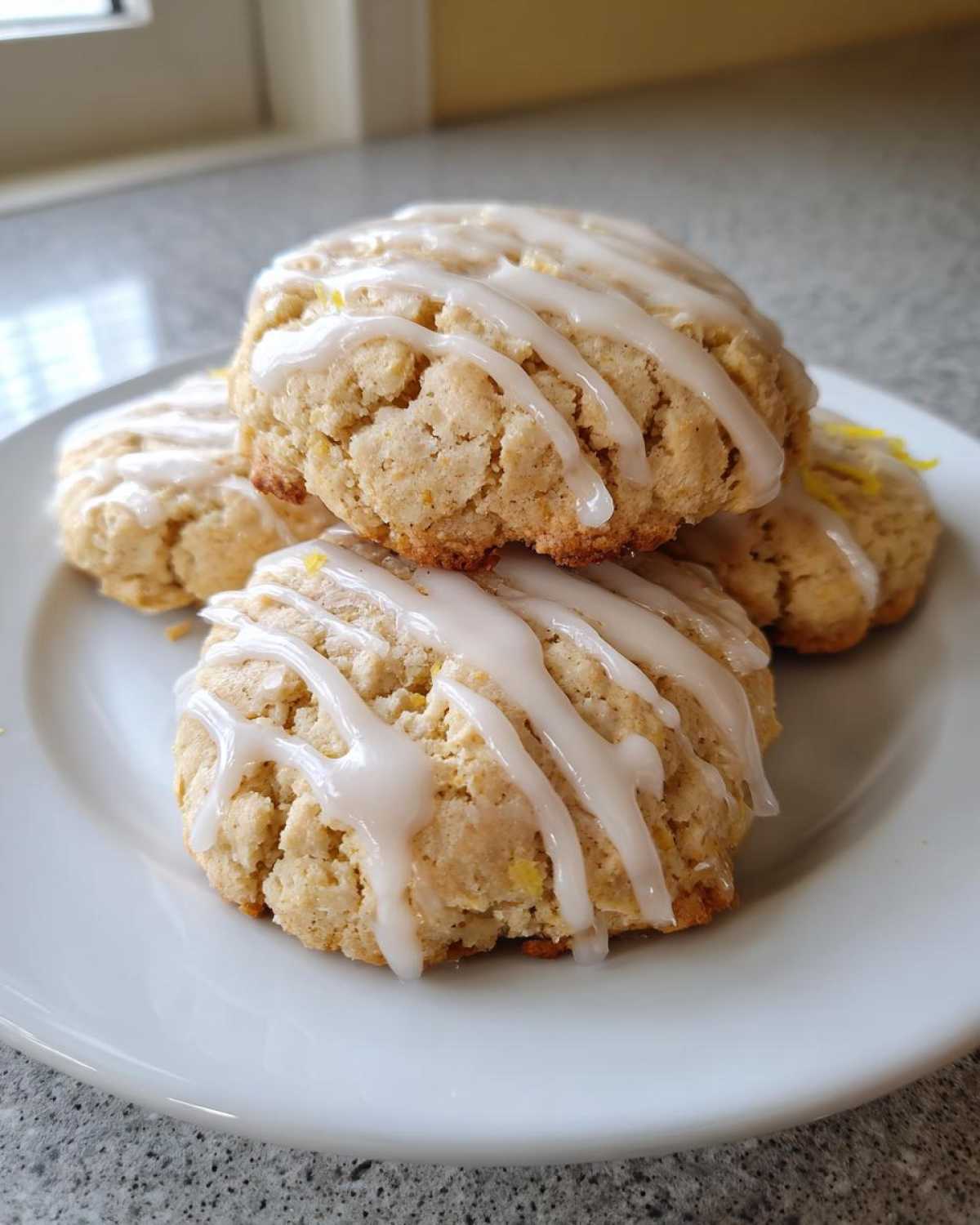 A stack of four Gluten-Free Lemon Ricotta Cookies drizzled with white lemon icing on a white plate.