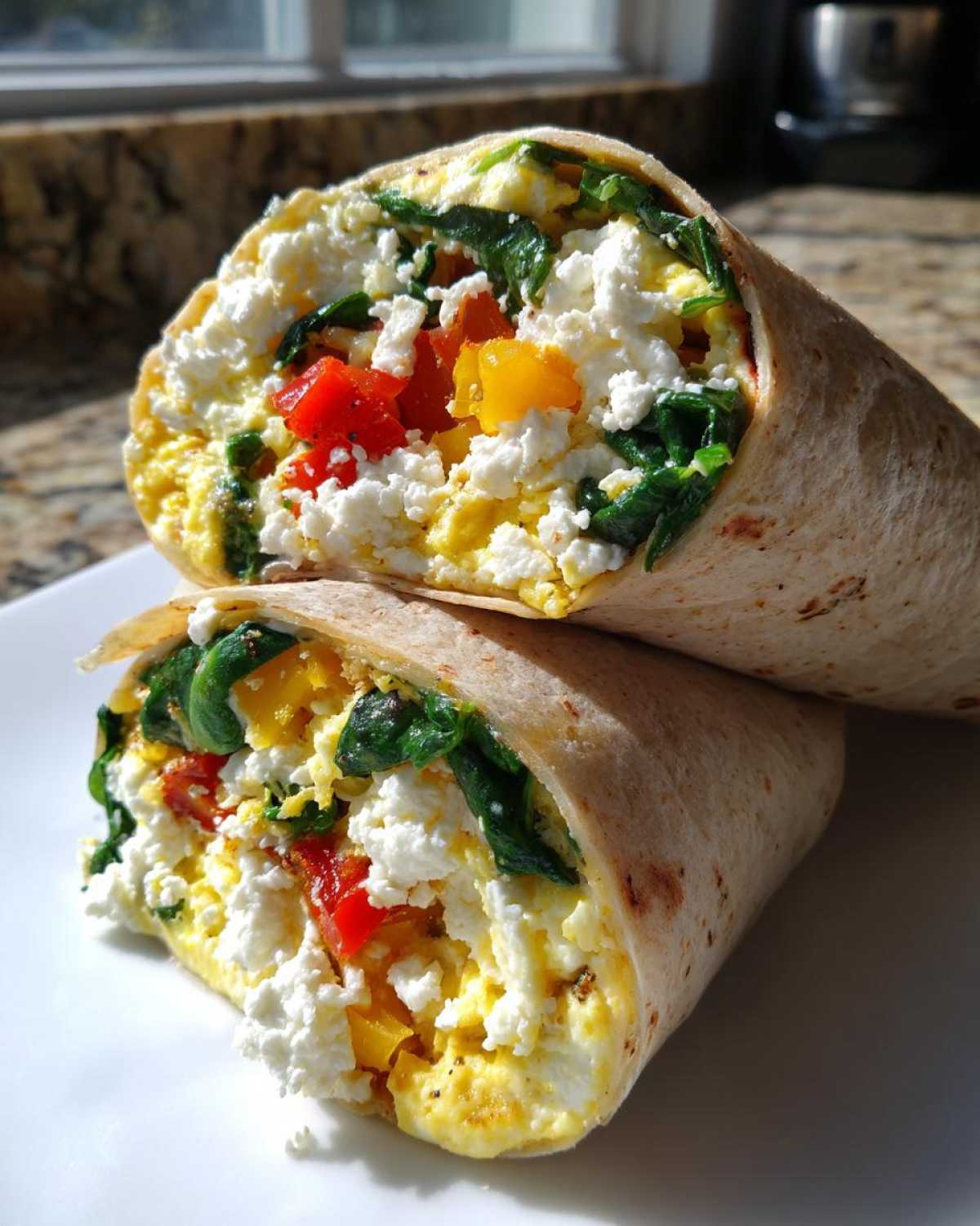 Two halves of a High-Protein Egg White Breakfast Wrap filled with egg whites, feta cheese, spinach, and peppers.