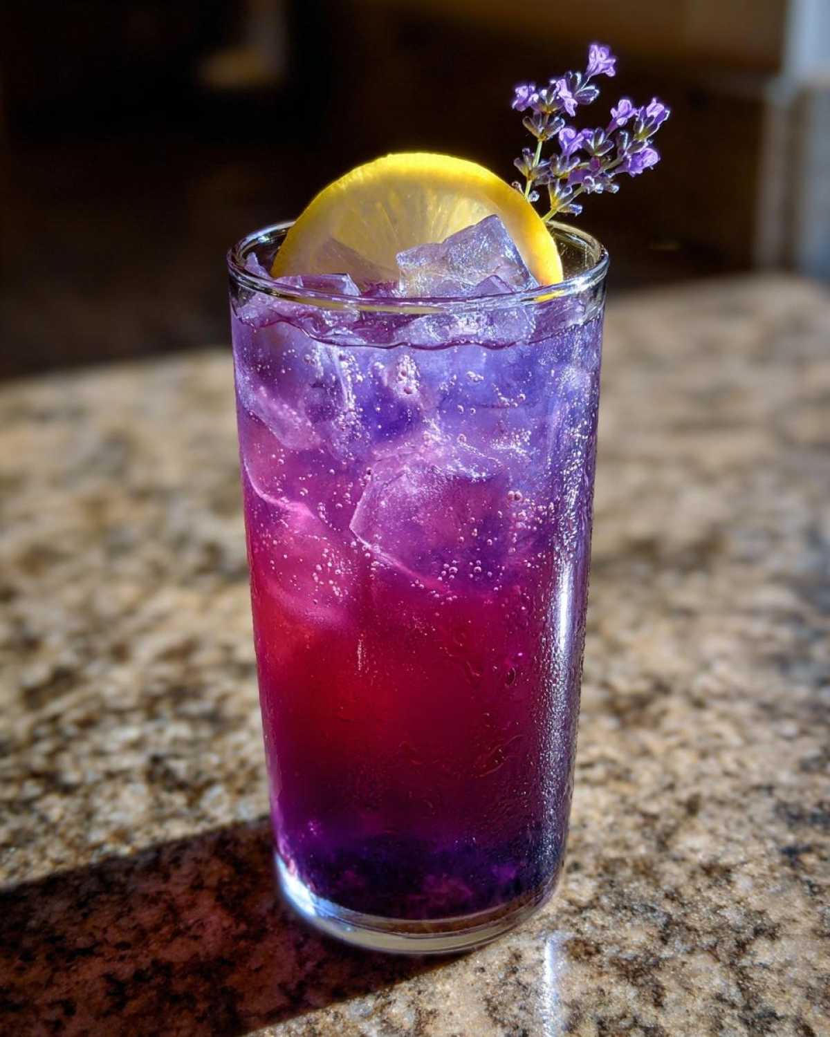 Close-up of vibrant Iced Blueberry Lavender Lemonade showing purple and pink layers, ice, and garnished with lemon and lavender sprigs.