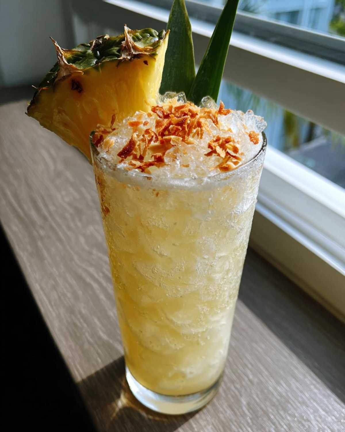 A tall glass filled with an Iced Pineapple Coconut Mocktail, topped with crushed ice and toasted coconut flakes.