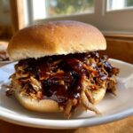 Close-up of a delicious Instant Pot BBQ Pulled Chicken Sandwich piled high with shredded chicken and rich BBQ sauce on a soft bun.