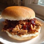 A close-up of a juicy Instant Pot BBQ Pulled Chicken Sandwich served on a soft bun with rich BBQ sauce.
