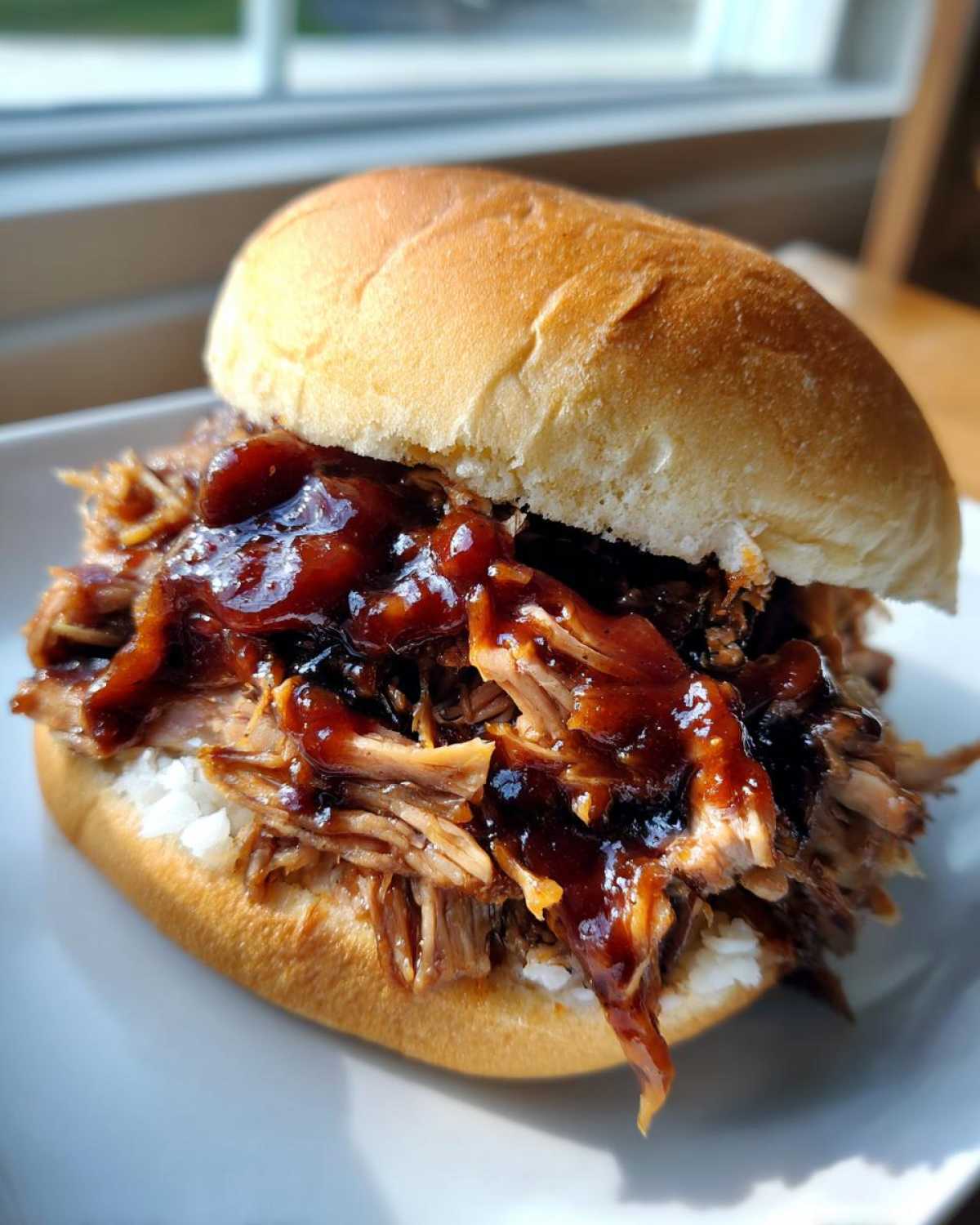 A close-up of a juicy Instant Pot BBQ Pulled Chicken Sandwich piled high on a soft bun with glossy sauce.