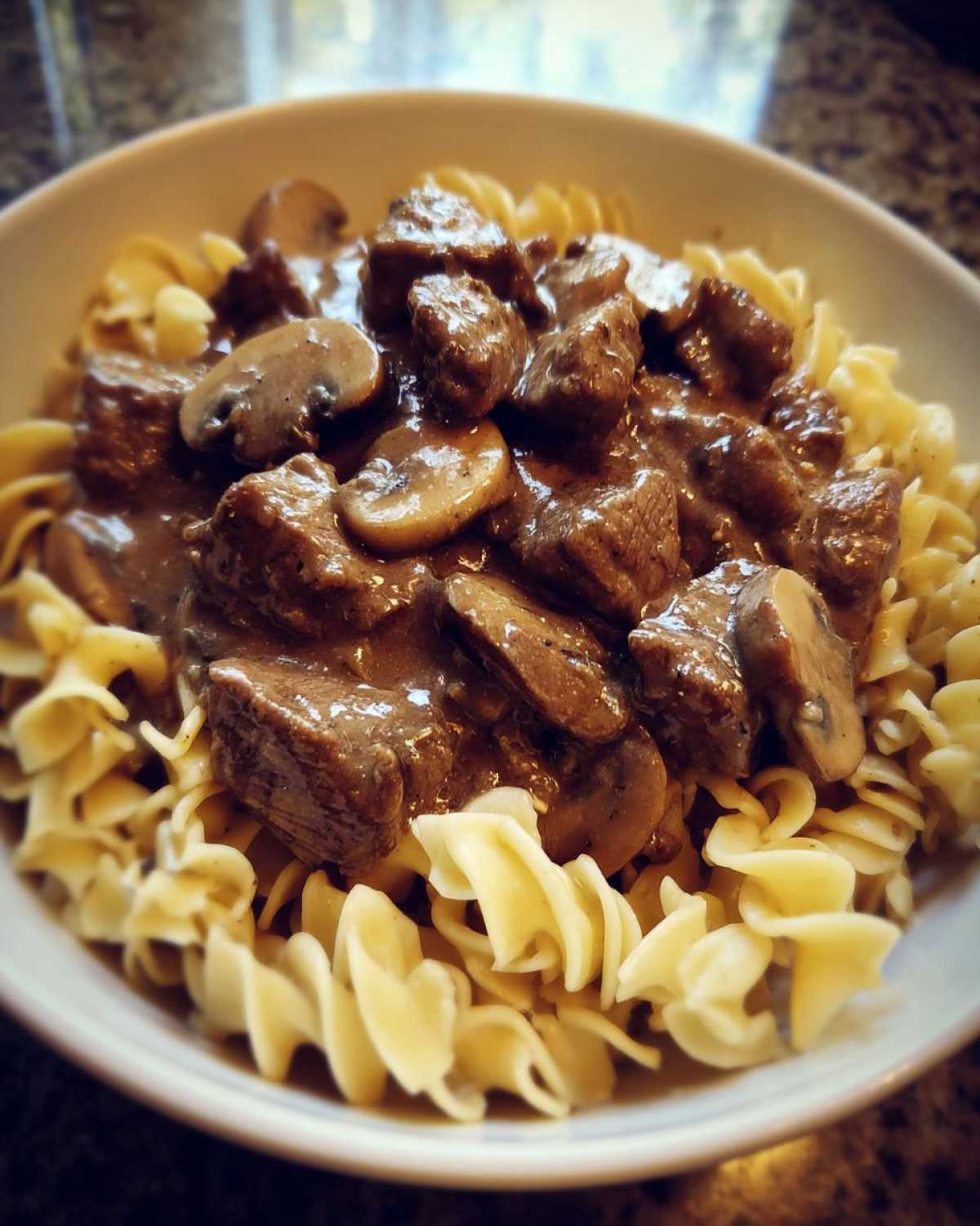 A close-up of Instant Pot Beef Stroganoff with Mushrooms served over egg noodles in a white bowl.
