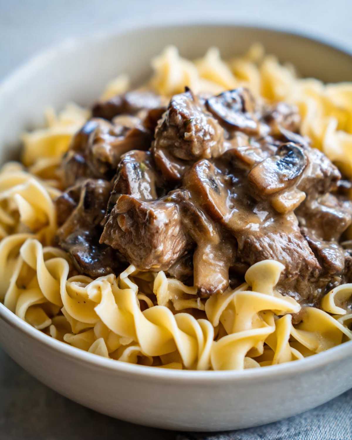 Close-up of Instant Pot Beef Stroganoff with Mushrooms served over wide egg noodles in a light bowl.