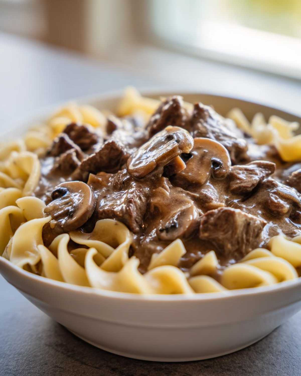 Close-up of a bowl of Instant Pot Beef Stroganoff with Mushrooms served over wide egg noodles.