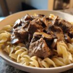 Close-up of a white bowl filled with Instant Pot Beef Stroganoff with Mushrooms served over egg noodles.