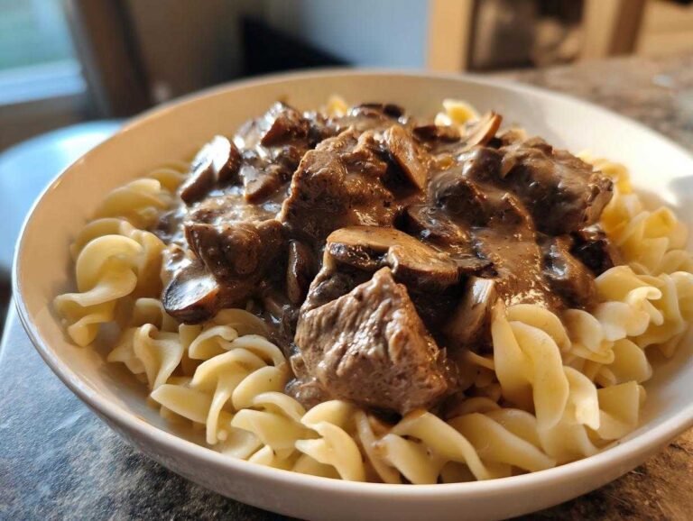 Close-up of a white bowl filled with Instant Pot Beef Stroganoff with Mushrooms served over egg noodles.