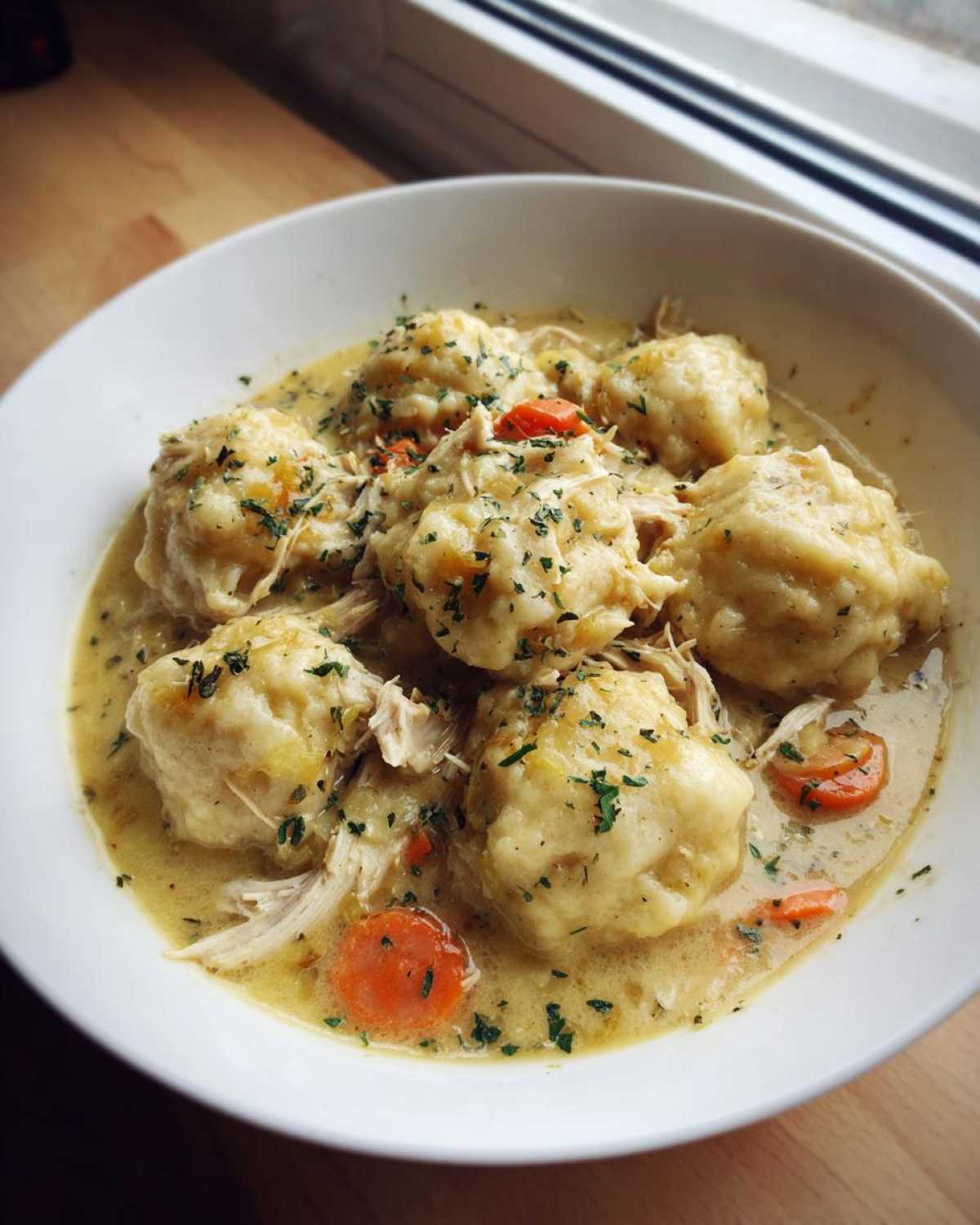 A close-up of a white bowl filled with creamy Instant Pot Chicken and Dumplings, topped with parsley.