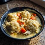 Close-up of a dark bowl filled with creamy Instant Pot Chicken and Dumplings, featuring large dumplings and bright carrots.