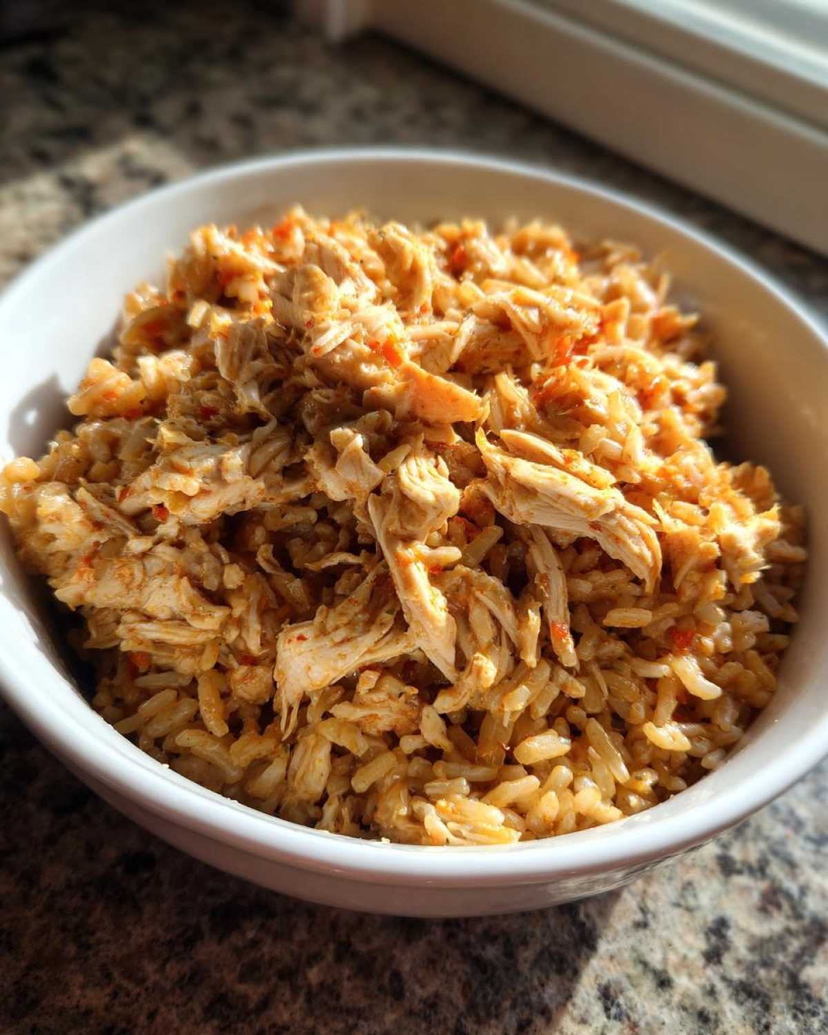 Close-up of seasoned shredded chicken mixed with brown rice in a white bowl, part of Instant Pot Chicken Burrito Bowls.