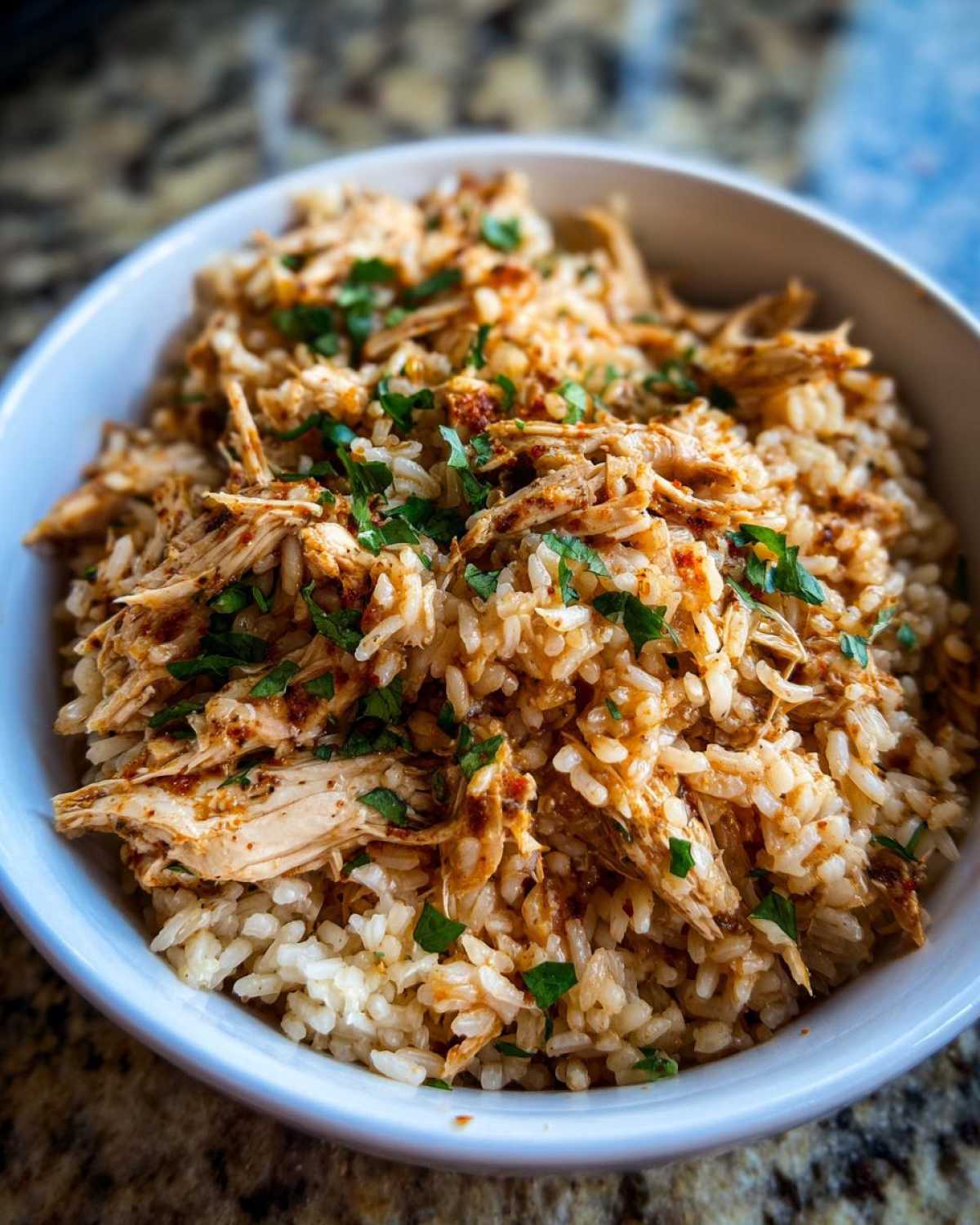 Close-up of Instant Pot Chicken Burrito Bowls with brown rice and shredded seasoned chicken, topped with cilantro.